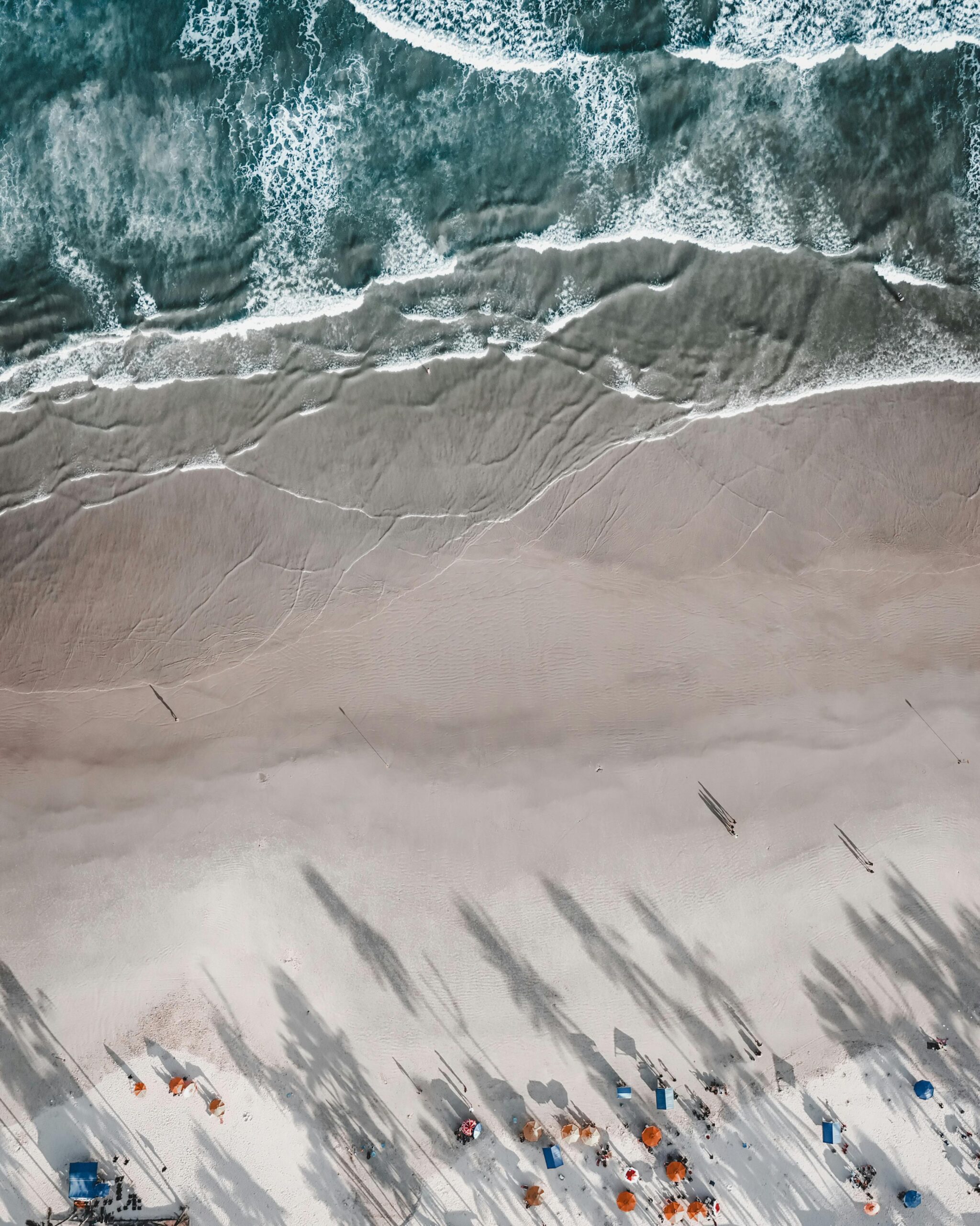 An aerial view of the beach waves, sand and people on the beach.